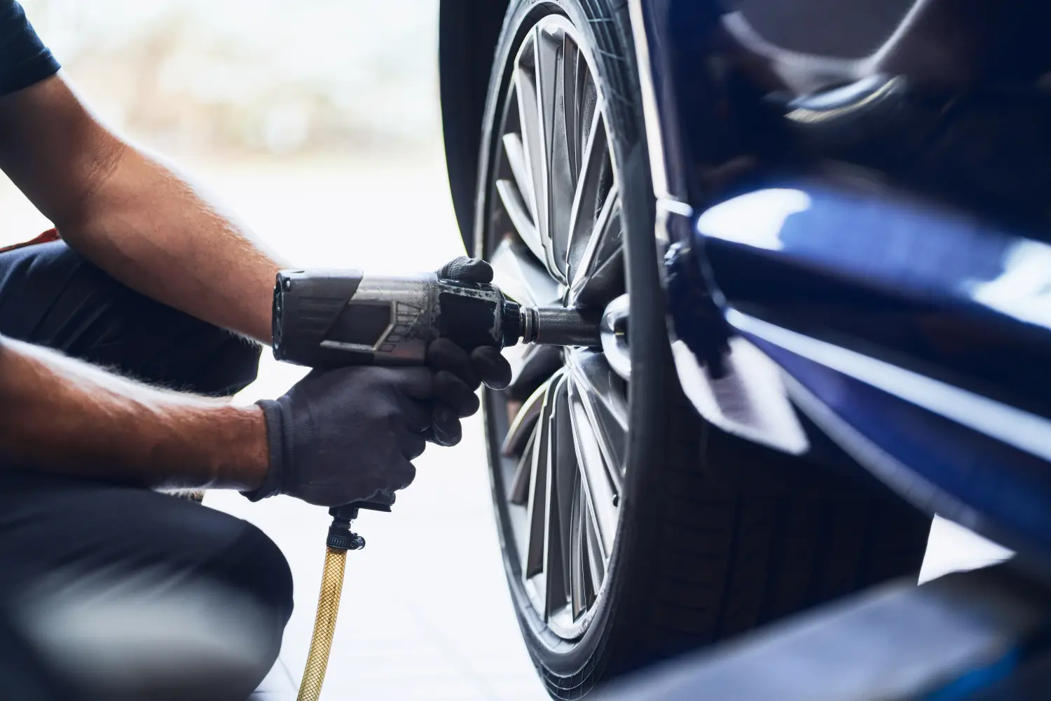 Reifenservice, Aufbereitung, A.P Detailing, Außenaufbereitung, Innenaufbereitung, Zusatzleistungen, Reifen Einlagerung, Reifenmontage, Reifenprüfung & Beratung, Reifenwechsel, Reifen wuchten, Nahaufnahme eines Automechanikers, der mit einem Druckluftschrauber einen Autoreifen in einer Autowerkstatt wechselt.